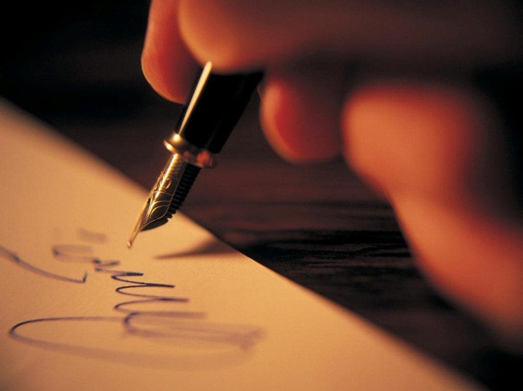 A hand using a fountain pen to write on paper.