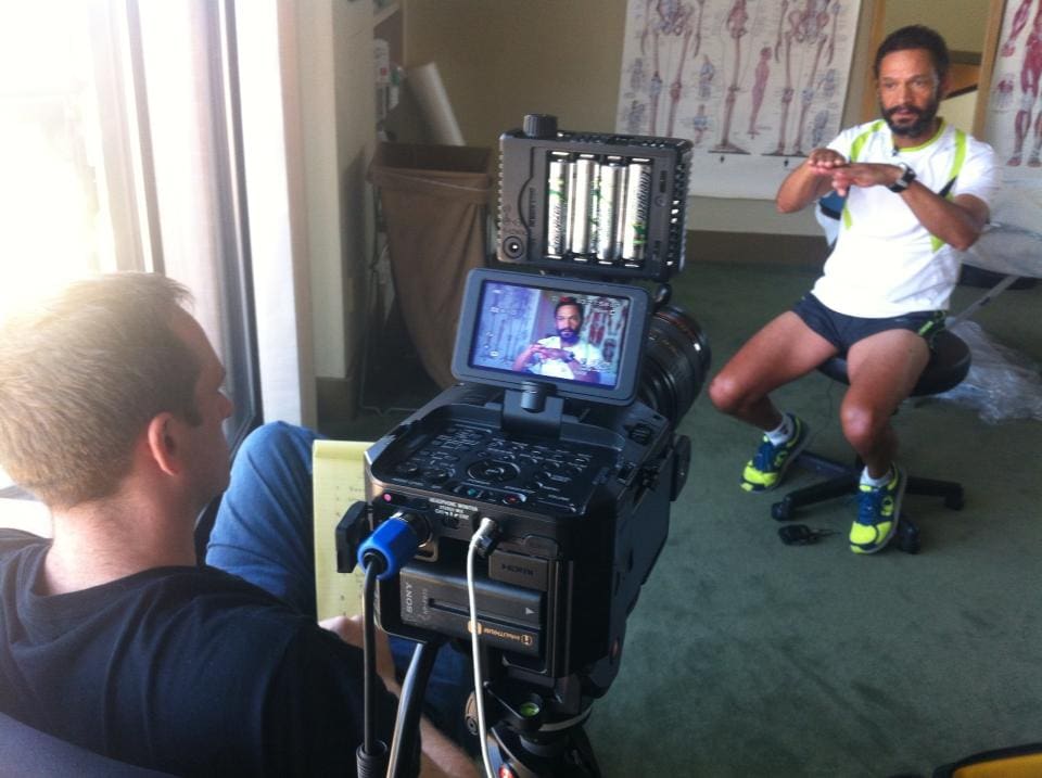 A camera operator filming a seated person speaking during an interview.