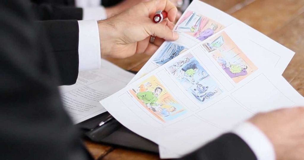 Hands holding illustrated storyboard sheets and a pen.