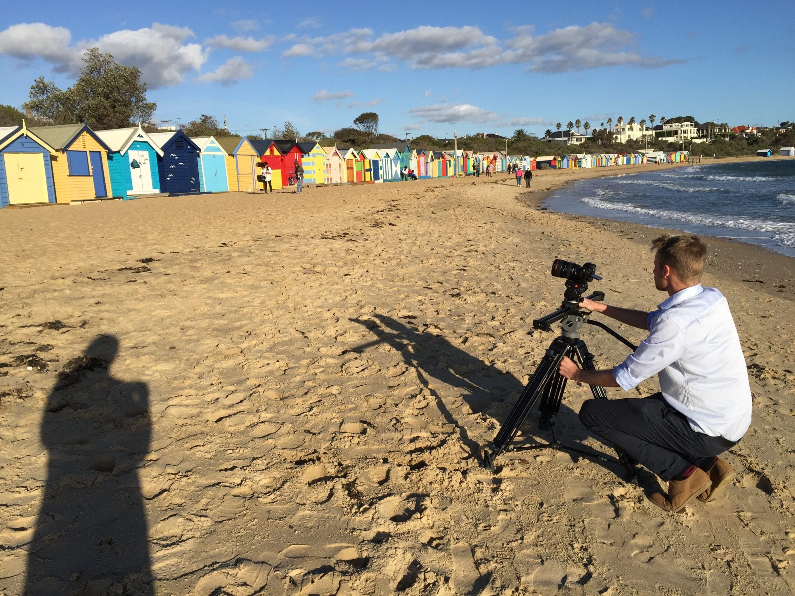 Dream Engine camera operator filming location footage beside Brighton Beach bathing boxes