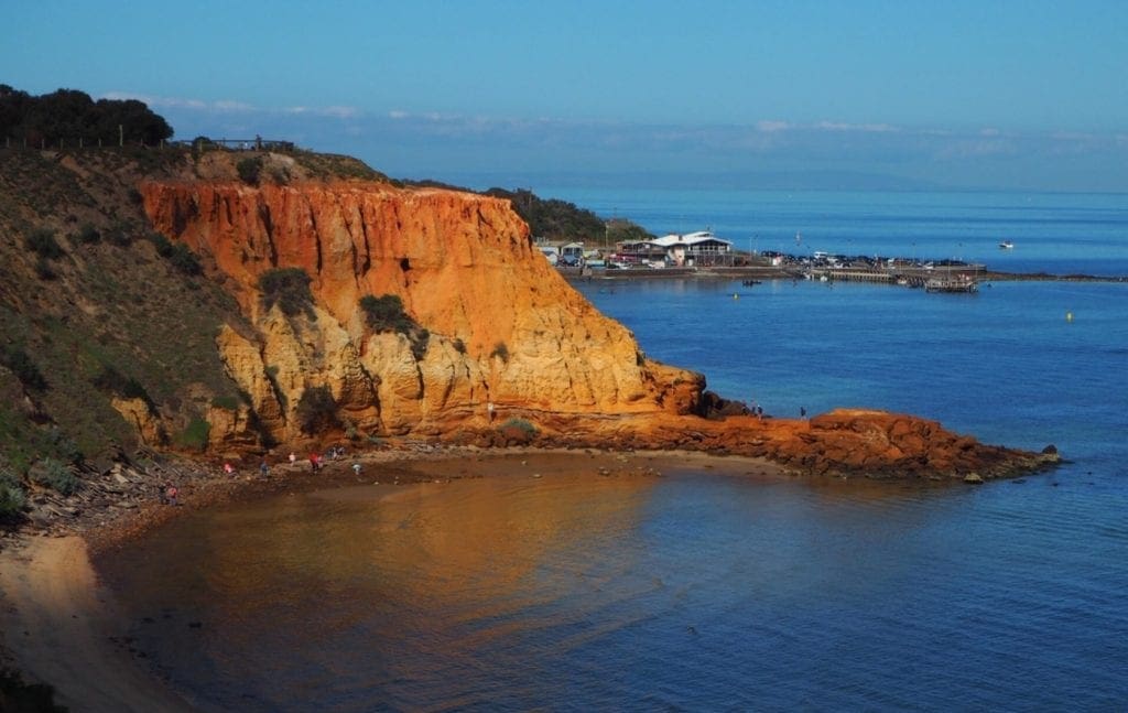 Red coastal cliffs, a beach and bay water at Red Bluff and Half Moon Bay.
