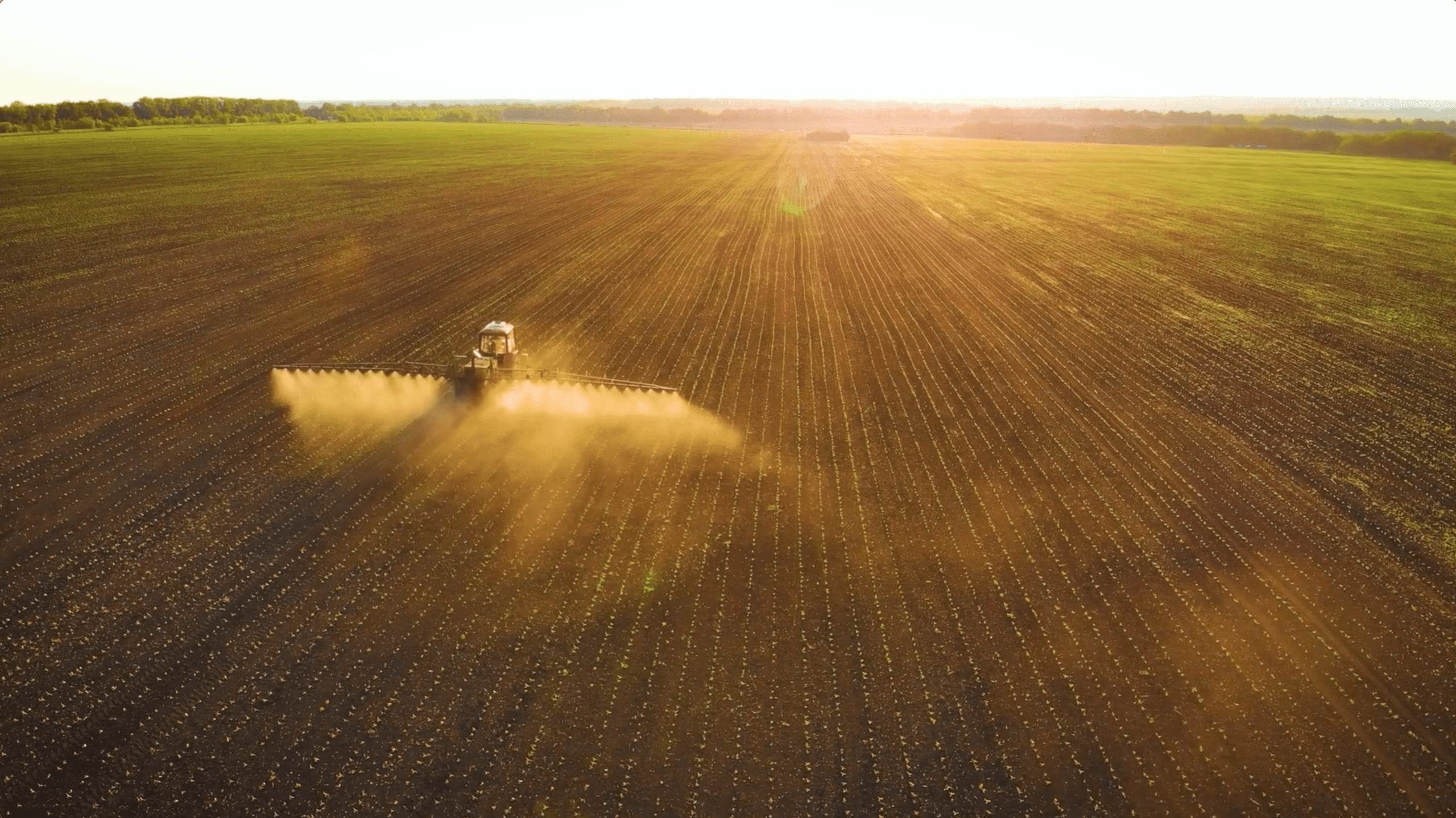 Aerial farming footage of a tractor working across a broad crop field