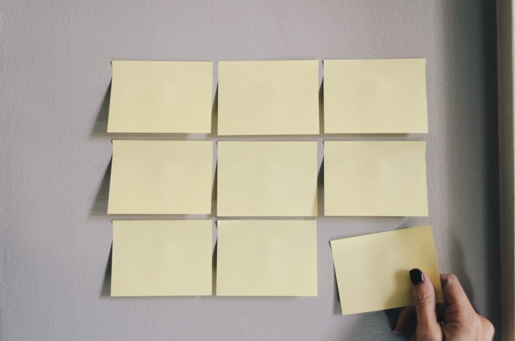 A hand arranging blank sticky notes in a grid on a wall.
