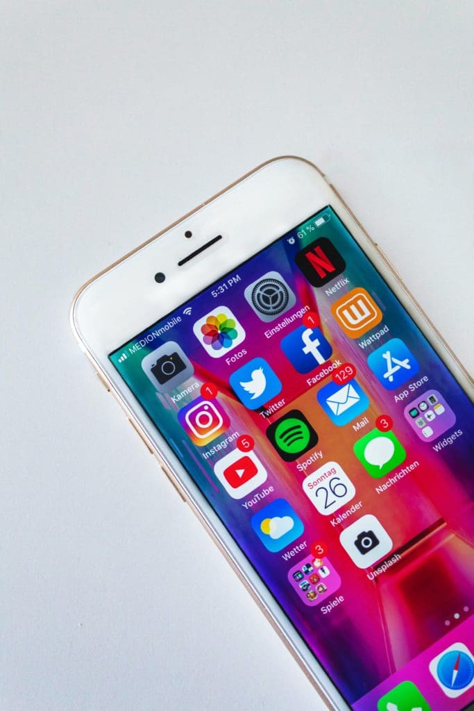 A white smartphone on a light surface, showing YouTube, Instagram and other apps on its home screen.
