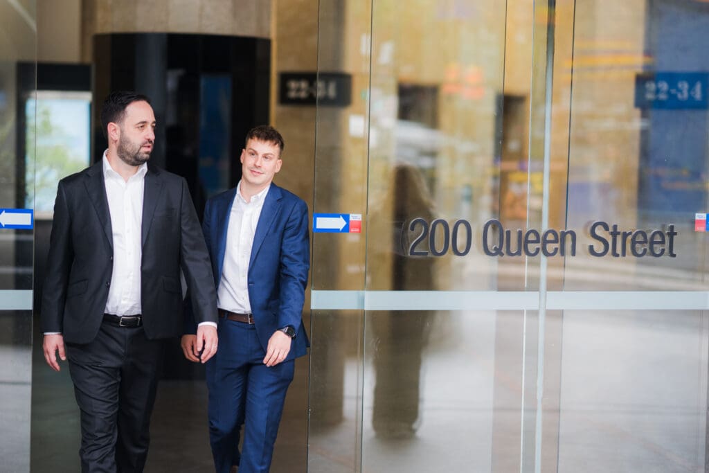 Two people in suits walking beside the glass entrance marked 200 Queen Street.
