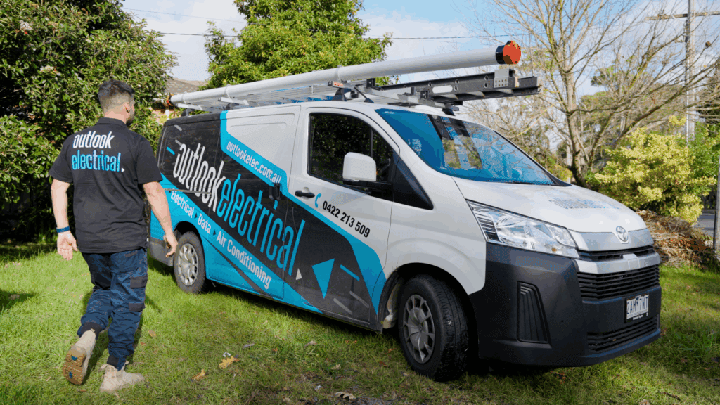 A person wearing Outlook Electrical clothing walking towards its branded work van.