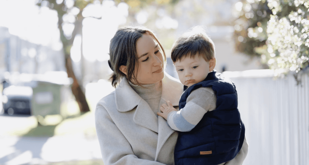An adult in a light coat holding a young child outdoors.