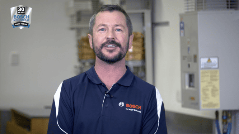 A speaker wearing a Bosch Hot Water and Heating shirt in an equipment room.