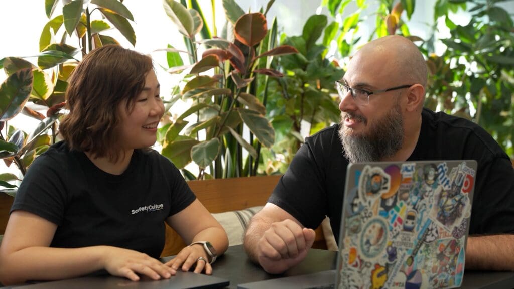 Two people in black shirts discussing their work beside a laptop.