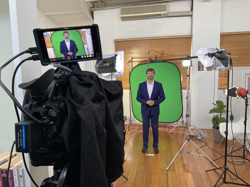 Presenter being filmed against a green screen with camera, monitor and lighting equipment for the OPP animated training modules.