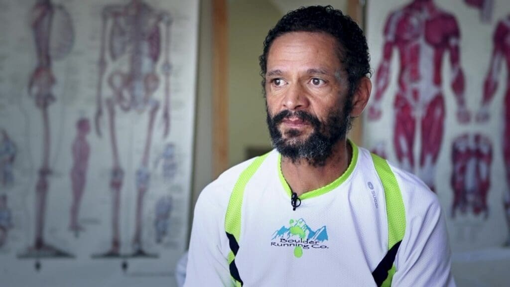 A man in a white and green shirt looking beside the camera during an interview.