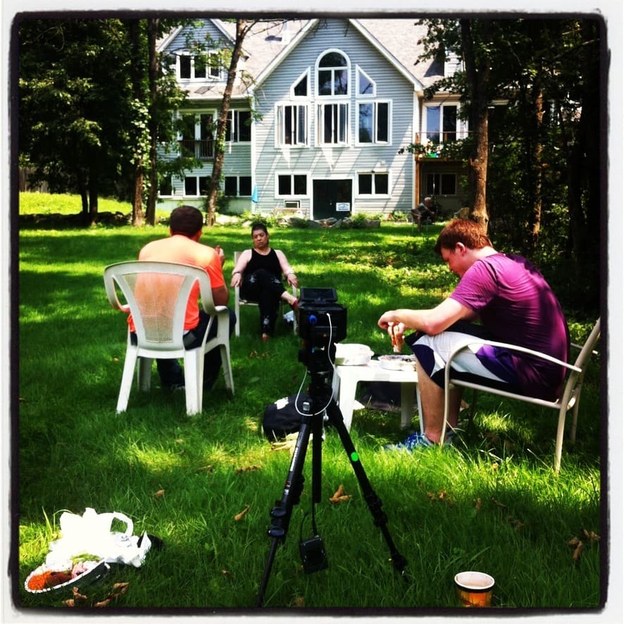 An outdoor interview with the interviewer seated beside a camera on a tripod.